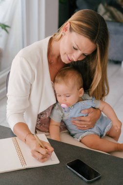 baby sleeping while mother writing notes with pen at home