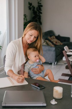 mother holding baby and working from home