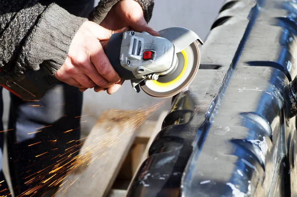 A man grinds a metal tank with a grinder