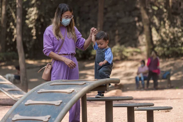 Baby boy climbing steps at the park holding his mother\'s hand