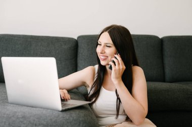 smiling woman talking on phone while using laptop