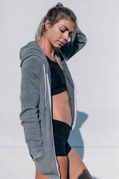 Woman with abs wearing activewear and zip up jacket leaning agai