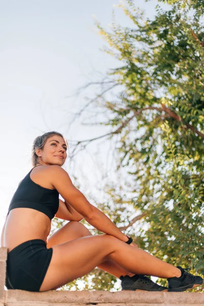 Woman with abs wearing black activewear sitting on brick wall by