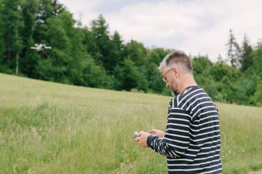 man flying drone watching remote control console in forest