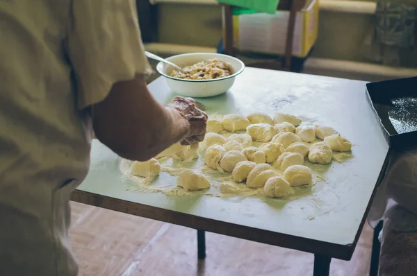 Old woman making dough balls for patties with flour on kitchen table
