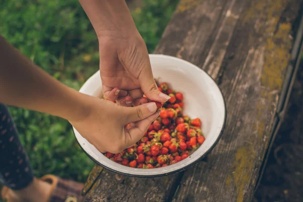 Girll's hands taking fresh strawberries to eat, from tureen on old bench. Country vacances on open air