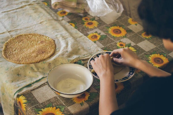 Girl's hands taking small pancake from a plate to eat with white sour cream in country kitchen