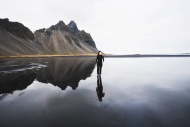 woman and her reflection on reflecting beach against mountains