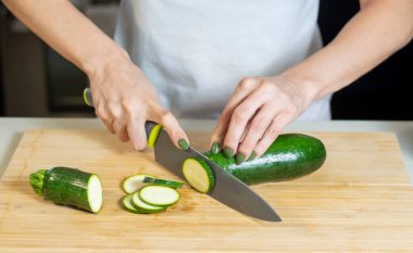 Genç kadın ellerinin evdeki tahta kesme tahtasıyla kabak kesmesine yakın çekim. Genç bayan sağlıklı yemek hazırlıyor..
