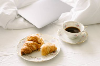 Overhead view of drink served in cup by smart computer laptop, coffee cup and croissants