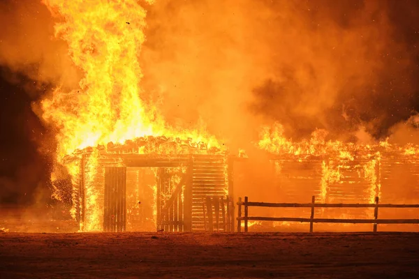 A small wooden house burning at night, sparks fly in the sky