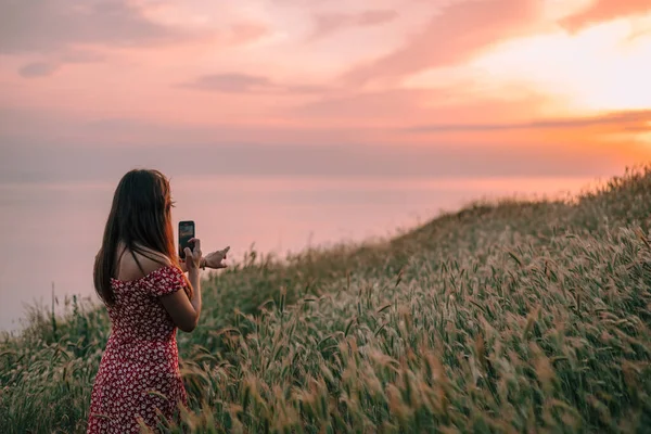 年轻女子在山上用智能手机拍摄日落 — 图库照片