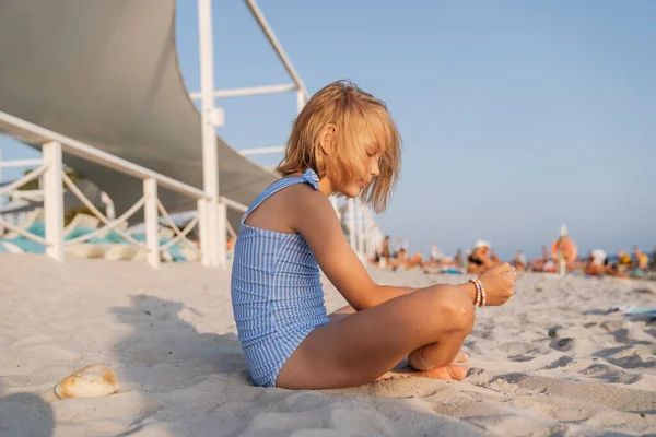 Kumsalda mayo giymiş kumla oynayan bir kız..