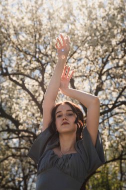 Bayan mavi elbiseli çiçek açan bir bahçede kollarını kaldırdı..