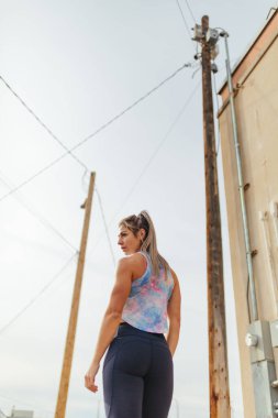 Back of blonde female standing outside in sun wearing tie dye sh
