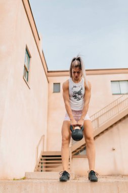 young female outside doing kettlebell deadlifts by old building