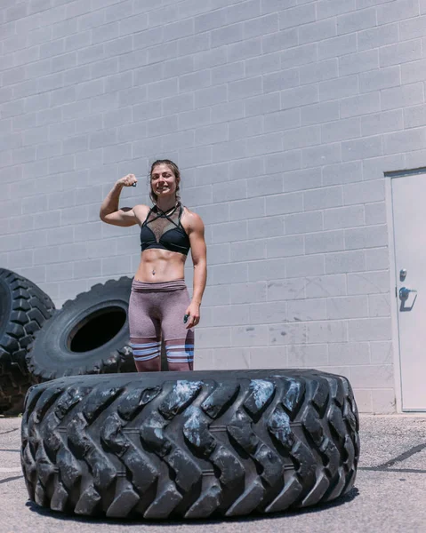 Fit athletic woman smiling flexing muscles after a tire flip out