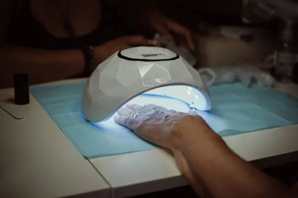 Hand under lamp for drying. Manicure in beauty salon