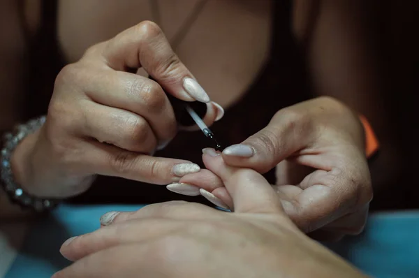 Manicurist hands paint nails on client\'s hand with varnish