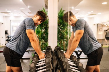 Strong sportsman taking dumbbells from rack