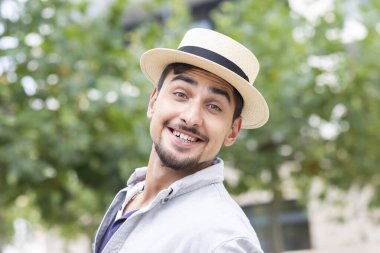 young man with summer hat in front of trees in a city