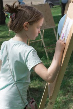 Kız bir yaz günü açık havada sehpada resim yapıyor.