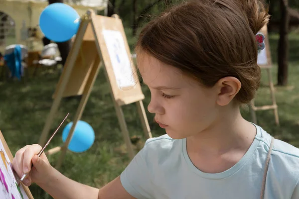 Girl paints on an easel outdoors on a summer day