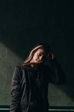 Siyah ceketli genç bir kız binanın duvarında dikiliyor.