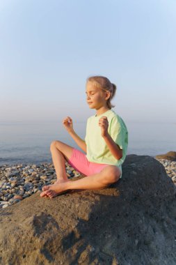 Kız sahilde oturuyor ve yoga yapıyor, meditasyon yapıyor..