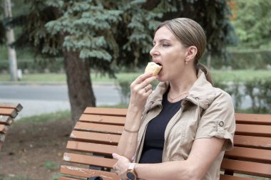 Kadın parkta dinleniyor, bankta tek başına oturuyor ve dondurma yiyor..