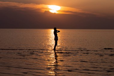 A woman stands in the sea at sunset