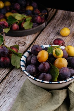 Tahta zemin üzerinde açık seramik tabakta taze erikler.