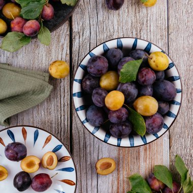 Tahta zemin üzerinde açık seramik tabakta taze erikler.