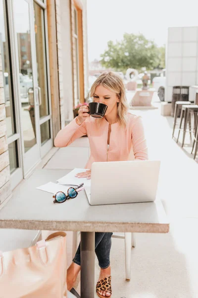 Young professional sips coffee while working on laptop outside