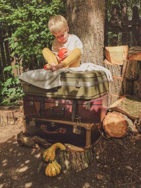 Küçük bir çocuk bir balkabağıyla oynuyor - antika bavulların üzerinde oturuyor