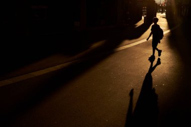 Gün batımında yolda gezinen tanınmayan bir çocuğun silueti.