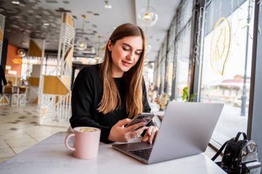 Penceredeki genç kız telefona bakıyor.