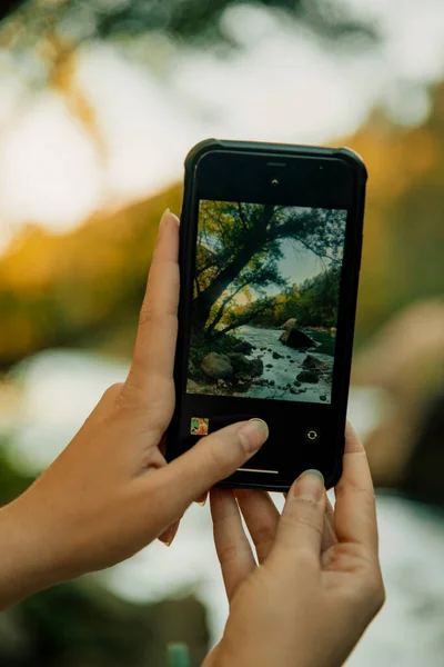一个用智能手机给河流景观拍照的女孩的手 — 图库照片