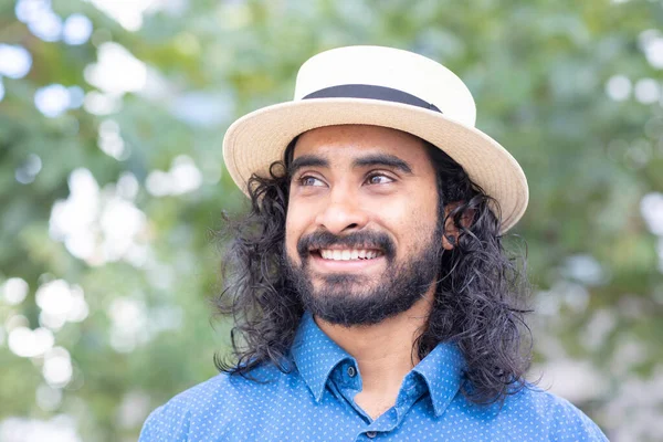 young man with beard and summer hat outside laughing