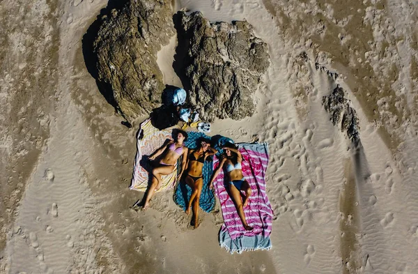 bird\'s eye view of three women lying on the sand on the beach