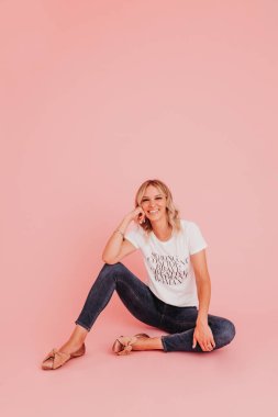 Genç bir bayan pembe stüdyo arka planında oturur ve kameraya bakar.