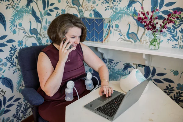 Mom talks on phone while pumping and teleworking at home.