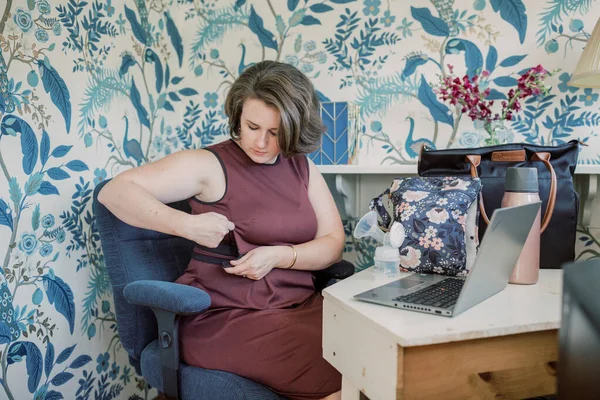 Working mother unzips pumping dress while sitting at desk.