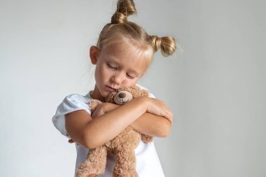 Küçük üzgün kız, gözlerini kapattı, oyuncak ayıya sarıldı.