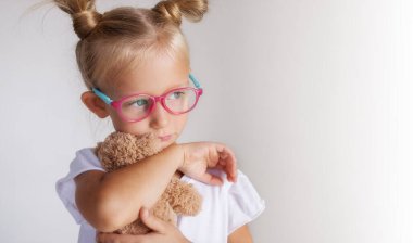 Yakın plan, gözlüklü ve elinde oyuncak olan bir kızın portresi.