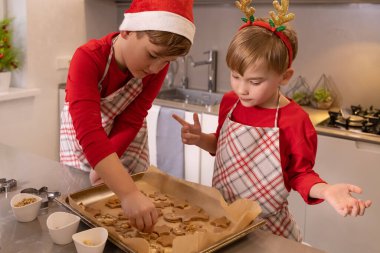 İki çocuk mutfakta Noel kurabiyesi pişirip yiyorlar.