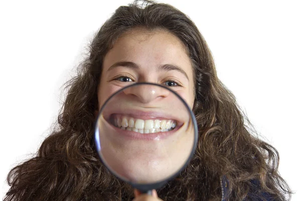 Menina sorrindo e mostrar dentes através de uma lupa sobre fundo branco — Fotografia de Stock