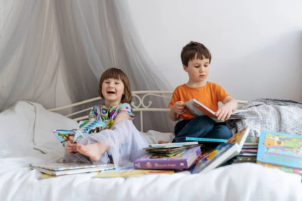 Dos hermanos leyendo libros en el sofá y riendo juntos — Foto de Stock