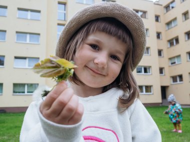 Şehrin arka planında elinde çiçek tutan gülümseyen küçük bir kızın portresi.