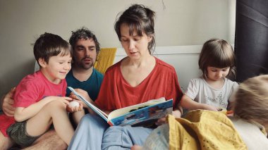 Mutlu ebeveynler yatakta oturan çocuklara kitap okuyor. Yüksek kalite fotoğraf